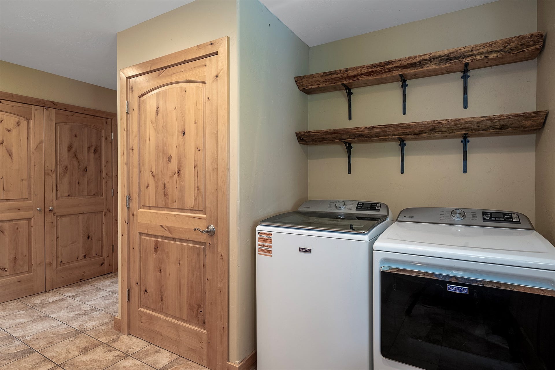 777 Mt Highway 83, Bigfork, MT 59911 Laundry area featuring a tiled floor, two natural wood doors, and two live-edge wood shelves with dark metal brackets
