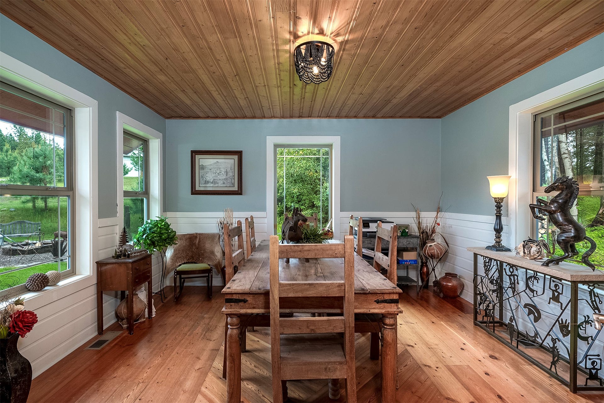 777 Mt Highway 83, Bigfork, MT 59911 Room featuring wood-finish flooring, wood-paneled ceiling, light blue walls, white wainscoting, and multiple windows