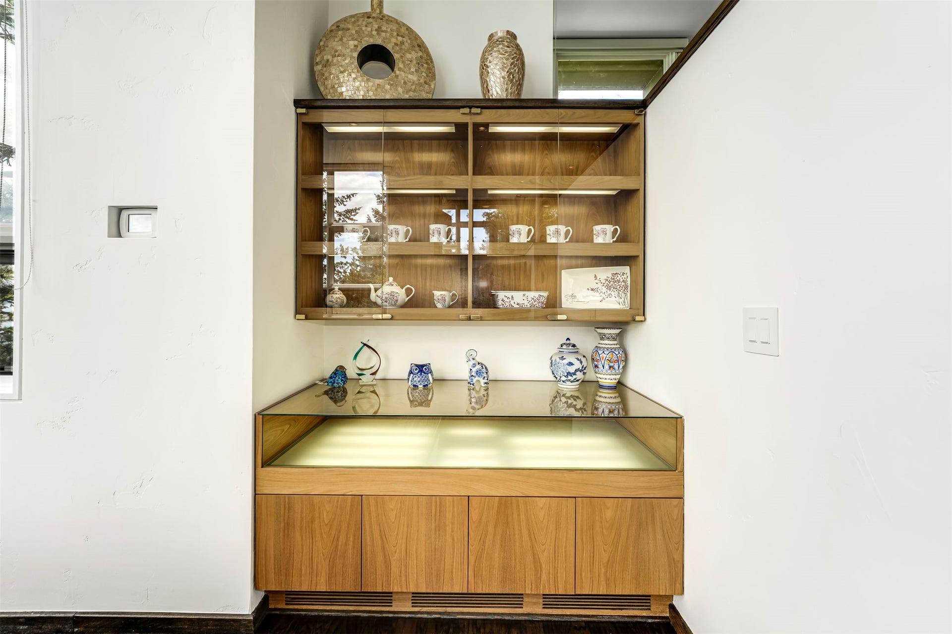 Integrated custom built-in cabinetry featuring display shelving with glass doors, recessed lighting, and a glass-top counter
