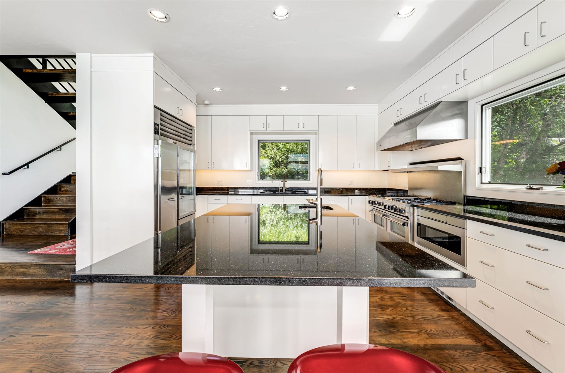 Modern kitchen featuring white cabinetry, dark stone countertops, stainless steel appliances, and wood-finish flooring