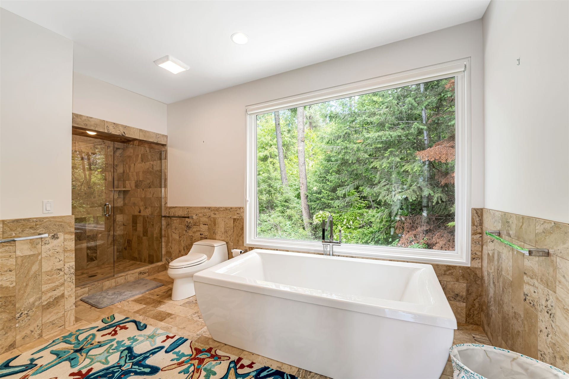 Freestanding soaking tub positioned before a large picture window, complemented by a spacious glass-enclosed shower