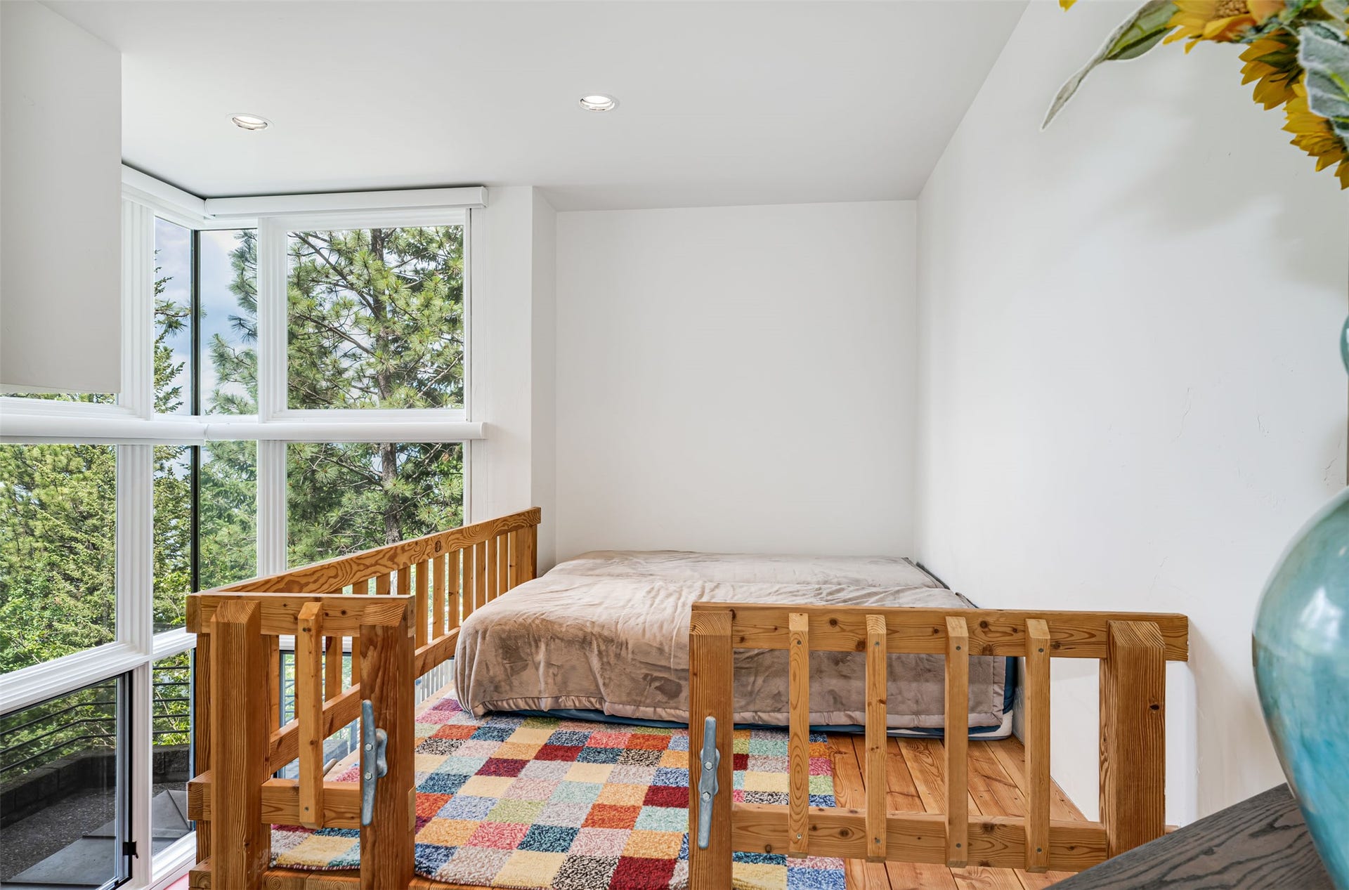 Loft sleeping area featuring expansive window wall, recessed lighting, and natural wood railing