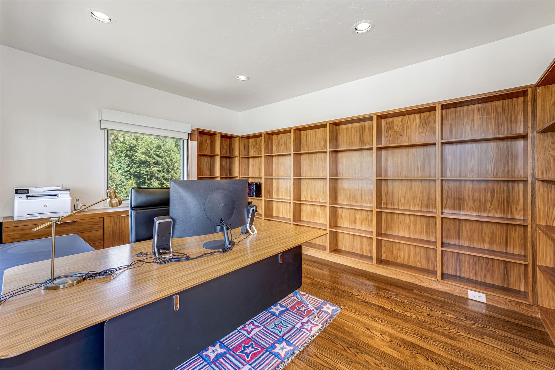 Dedicated office space near primary bedroom featuring extensive built-in wood shelving, wood-finish flooring, and recessed ceiling lighting.