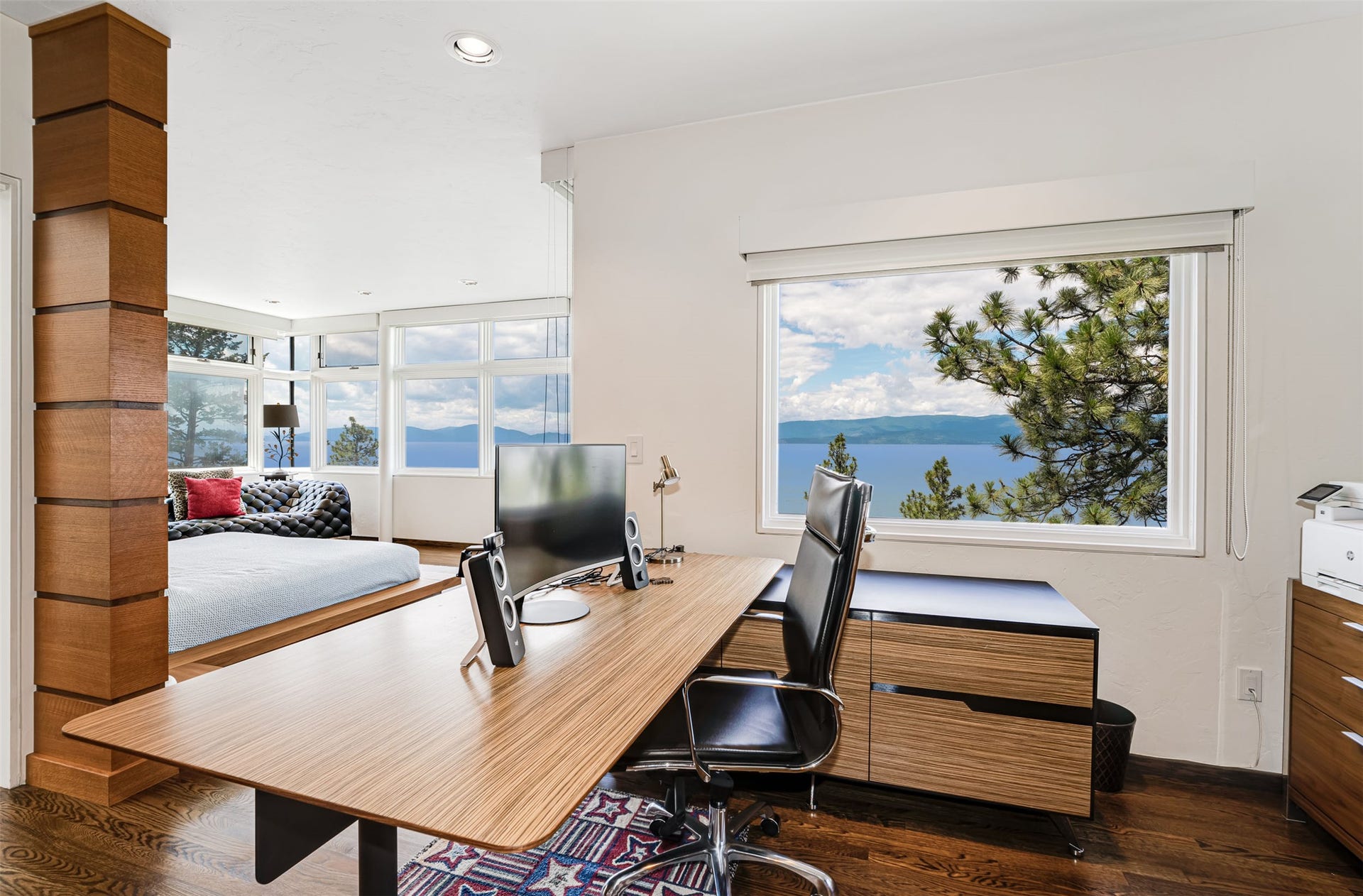 Home office featuring a wood-h desk and built-in storage cabinetry, hardwood flooring, and a large window overlooking a lake and distant mountains