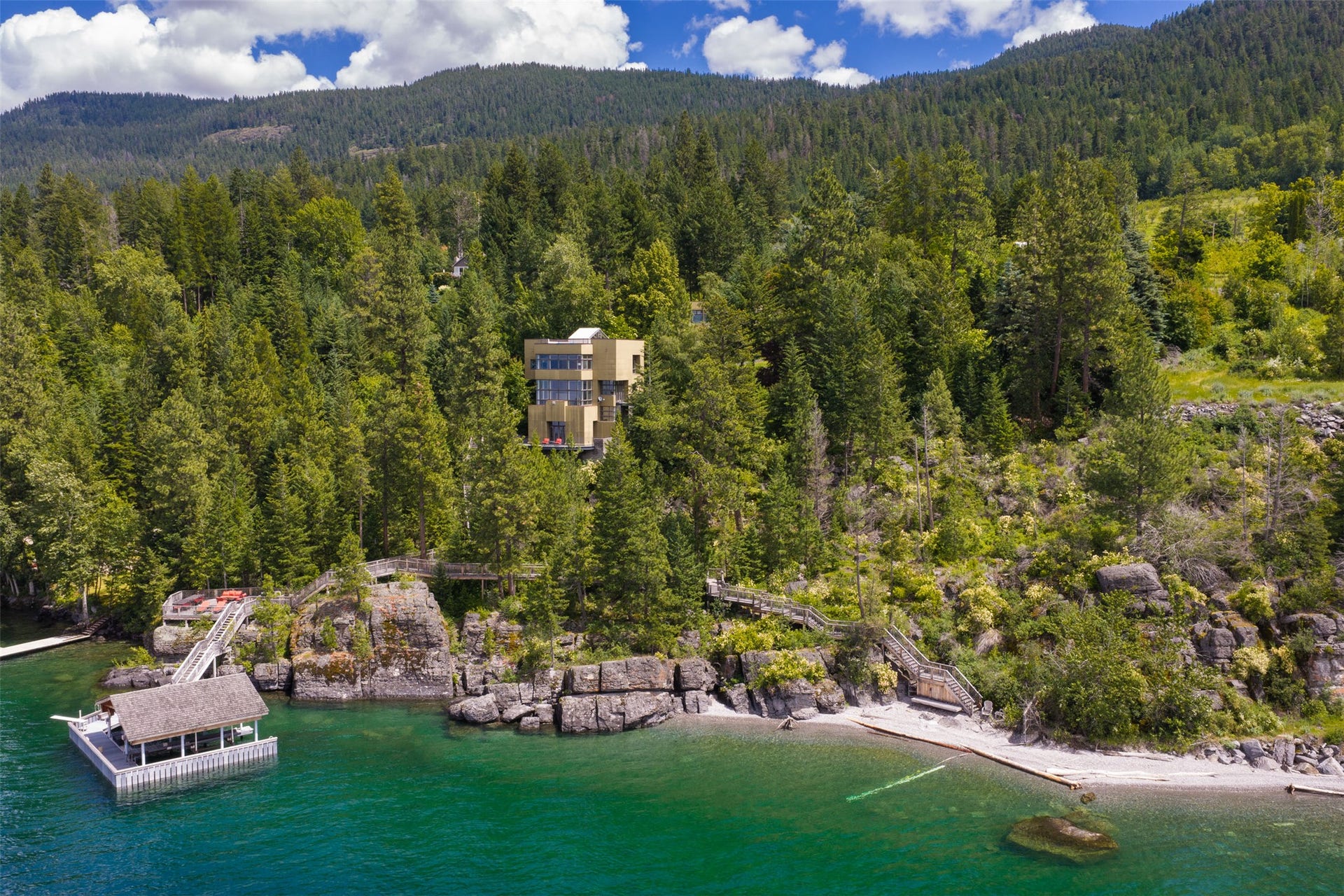 This Flathead Lake property is a multi-story contemporary home, 330 ft of shoreline, a covered boat slip, a private beach, and extensive natural landscaping with mature trees and rock outcroppings
