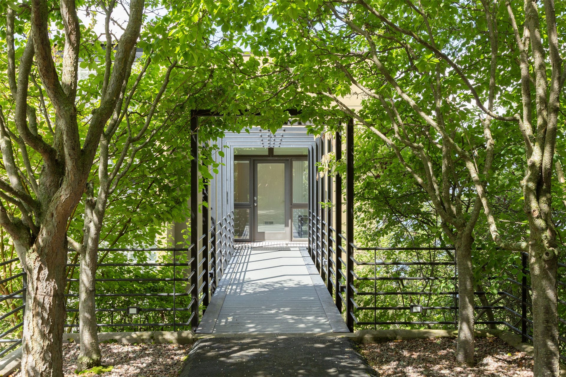 Lilac trees shade the steel bridge walkway to the front door of the home. Guests are invited to enter and experience this marvelous home on Flathead Lake!