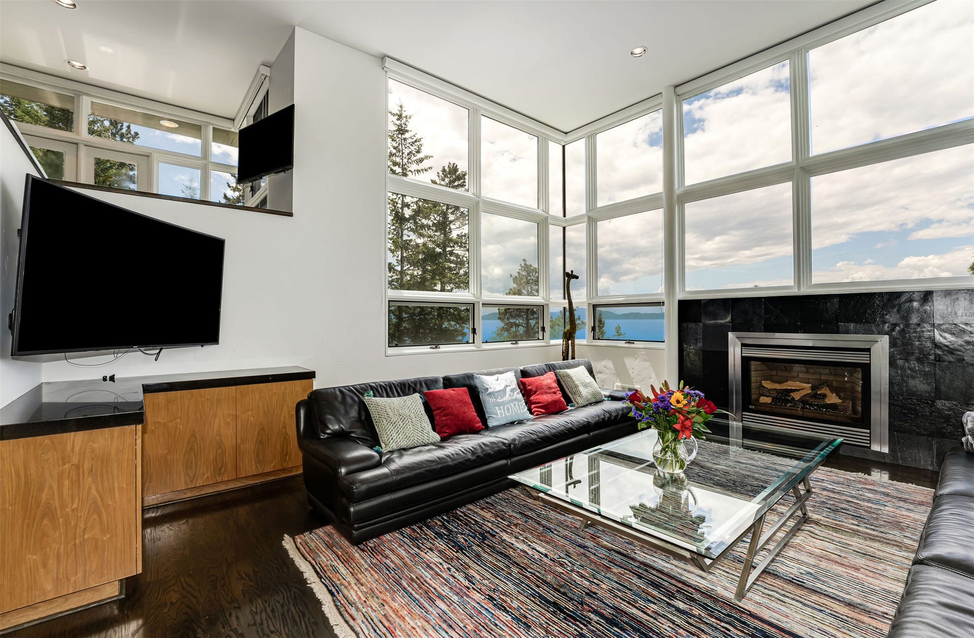 Living area with extensive window walls, dark wood-finish flooring, and a built-in fireplace featuring a dark stone surround