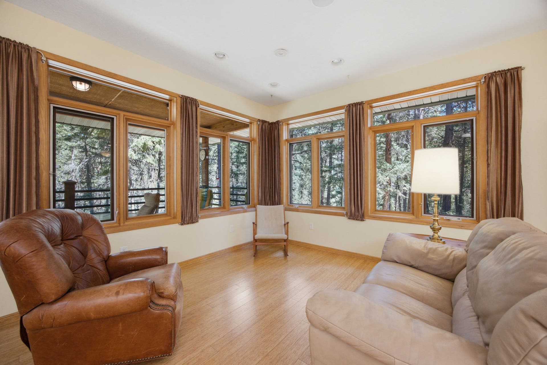 Walls of windows bring the outdoors in, filling the living room with natural light while showcasing the peaceful wooded setting. A warm, inviting space designed for both everyday living and entertaining.