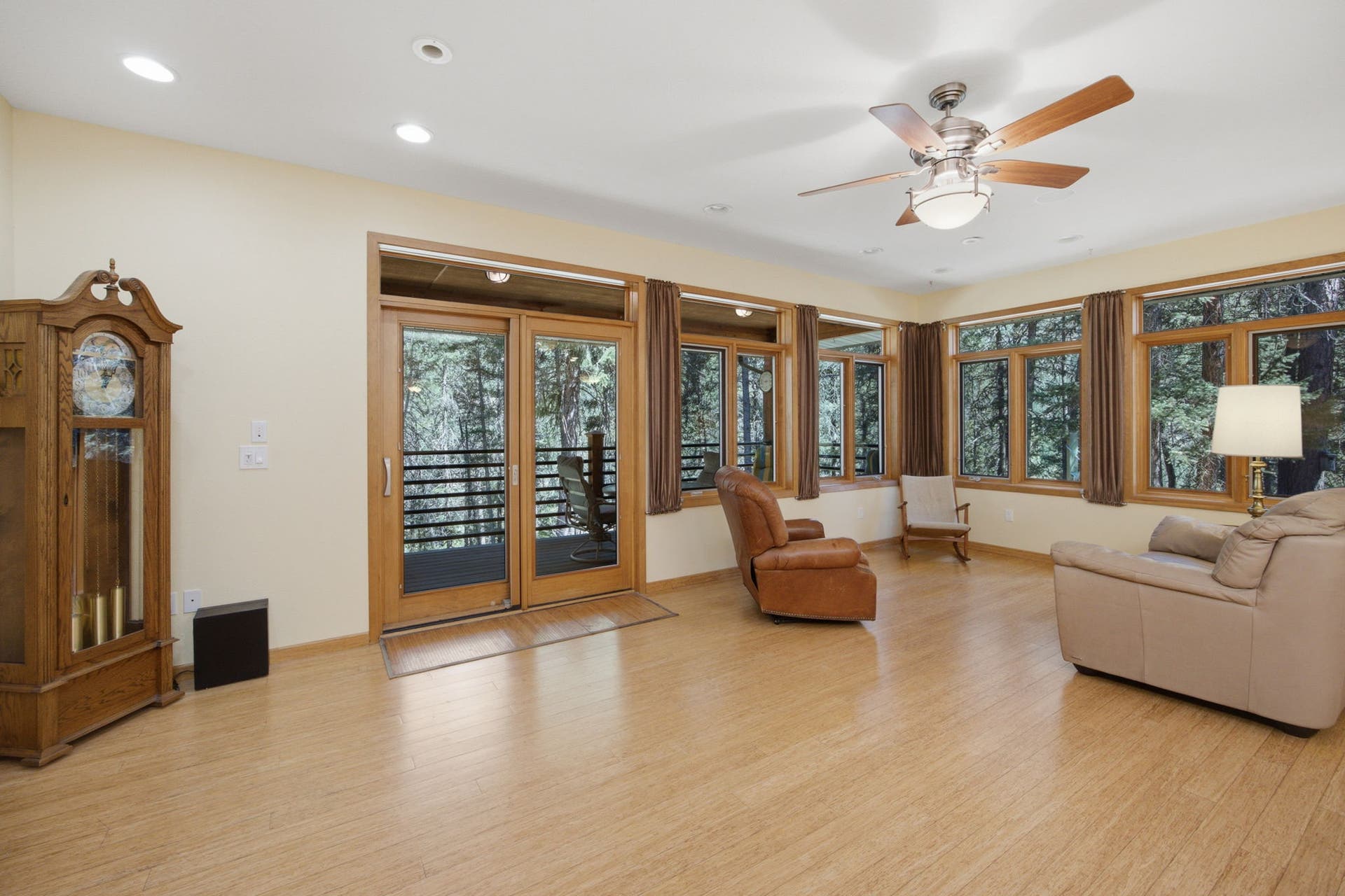 The heart of the home features an open-concept living space with rich bamboo flooring, expansive windows, and abundant natural light. Framed by towering pines and peaceful views, this inviting gathering area seamlessly connects to the kitchen and dining spaces.