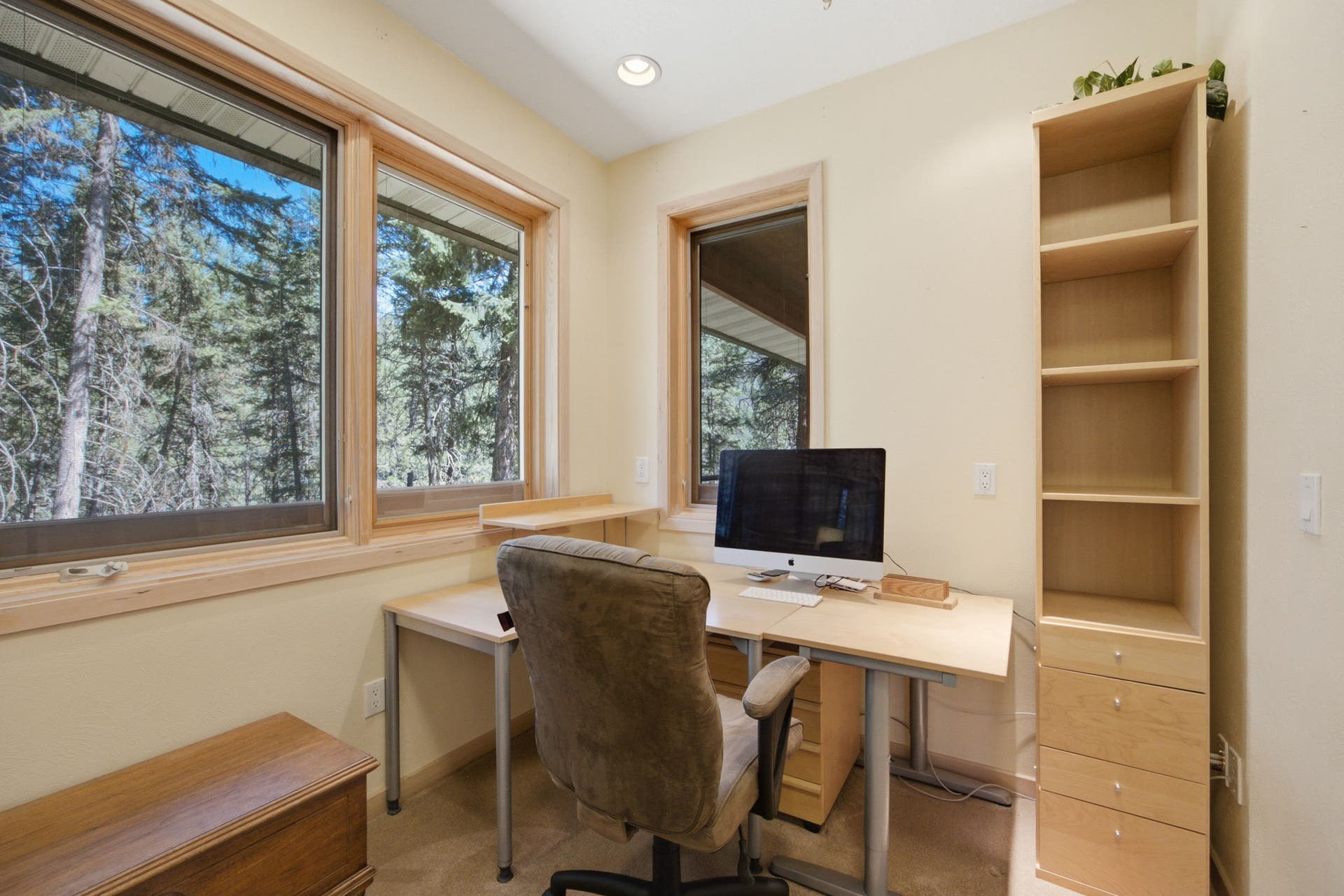 A bright home office with built-in shelving and large windows provides an ideal workspace for remote work, hobbies, or a quiet reading room while enjoying views of the surrounding pines.