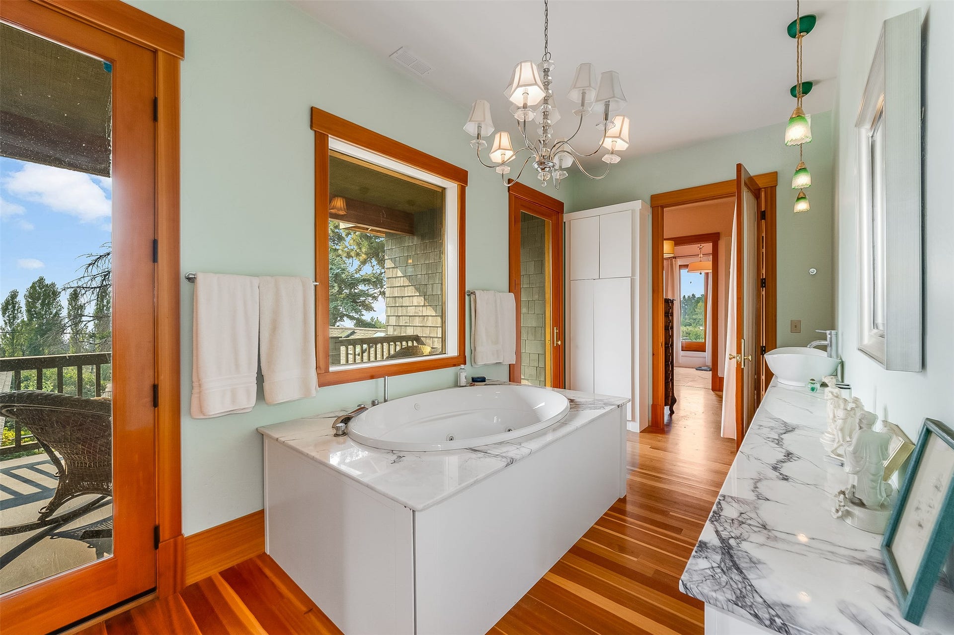 21848 Mt Highway 35, Bigfork, MT 59911 Spa-inspired bathroom featuring a jetted tub set in a white marble-look surround, wood-finish flooring, and a spacious vanity with a vessel sink