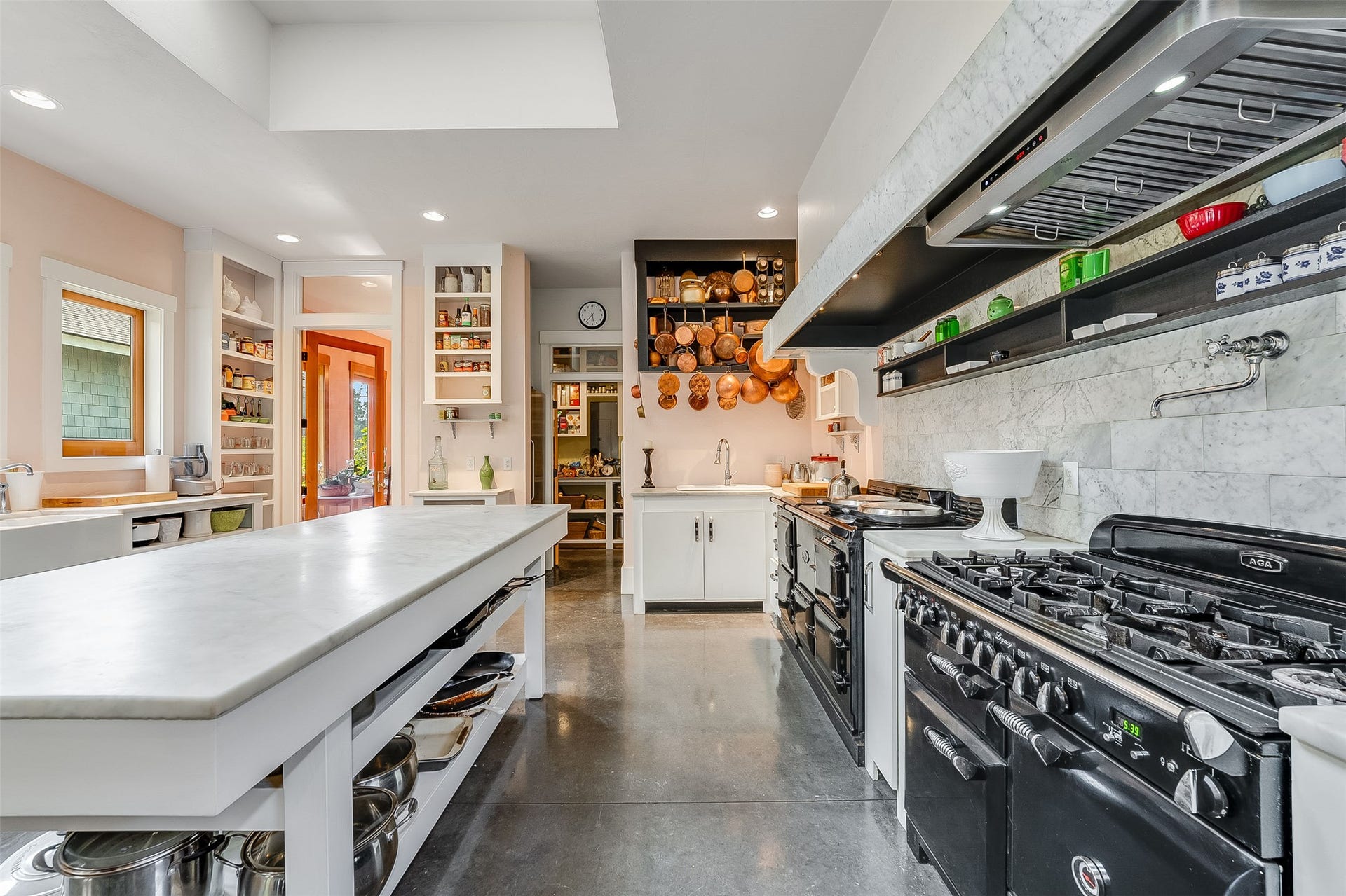 21848 Mt Highway 35, Bigfork, MT 59911 Gourmet kitchen featuring a substantial center island with a Cararra marble countertop, dual professional-grade Aga range and ovens, a large stainless steel range hood, white subway tile backsplash, and extensive open shelving.