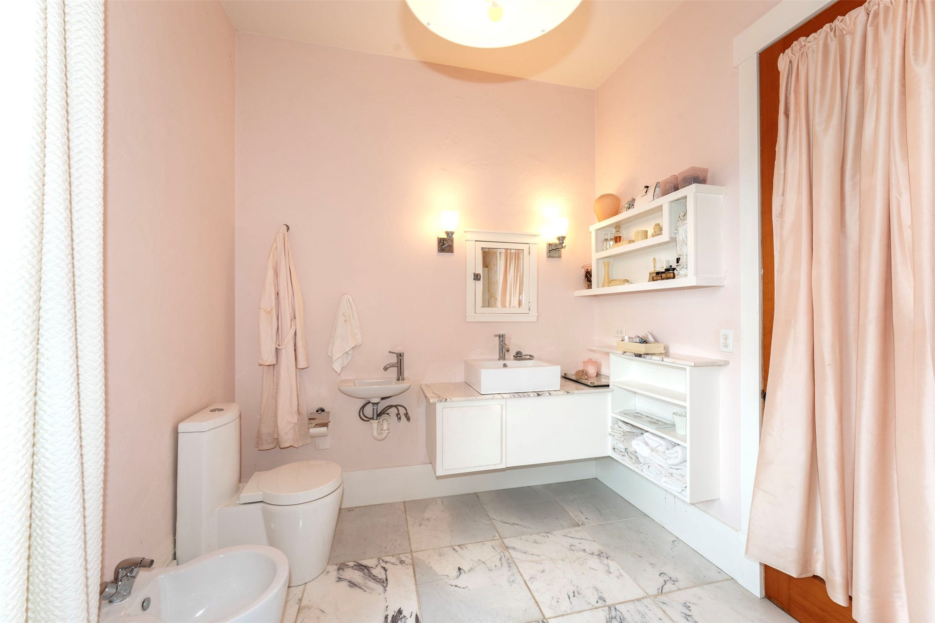 21848 Mt Highway 35, Bigfork, MT 59911 Bathroom featuring white marble-look tile flooring, a vessel sink with a white vanity, a wall-mounted mirror, and sconce lighting