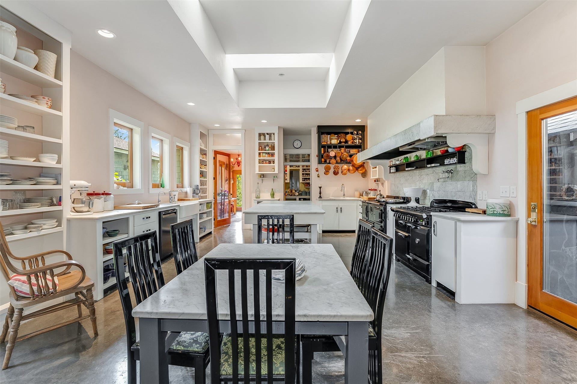 21848 Mt Highway 35, Bigfork, MT 59911 Breakfast area in spacious kitchen featuring multiple skylights and recessed lighting, extensive built-in shelving, white cabinetry, a large range hood, and concrete-finish flooring