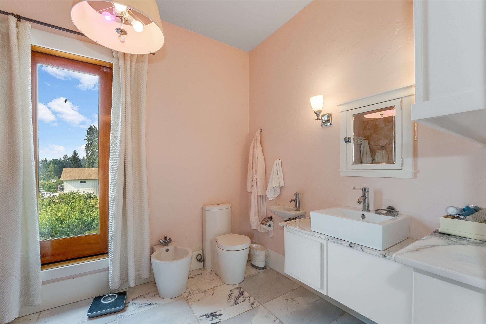 21848 Mt Highway 35, Bigfork, MT 59911 Bathroom featuring a wood-framed window, white marble-look flooring, a floating vanity with a vessel sink, a built-in medicine cabinet, and a wall-mounted sconce