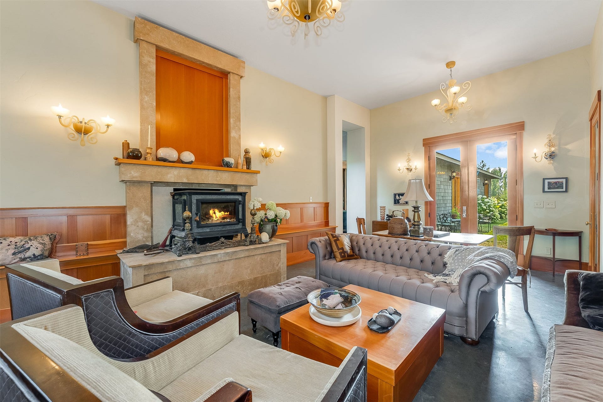 21848 Mt Highway 35, Bigfork, MT 59911 Spacious living area featuring a wood-burning stove set within a limestone fireplace, wood paneling, and wall-mounted sconces.