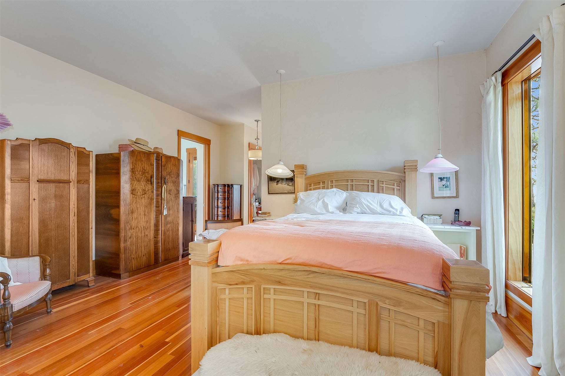 21848 Mt Highway 35, Bigfork, MT 59911 Bedroom featuring hardwood flooring, light-toned walls, a large window with wood trim, and a ceiling-mounted pendant light