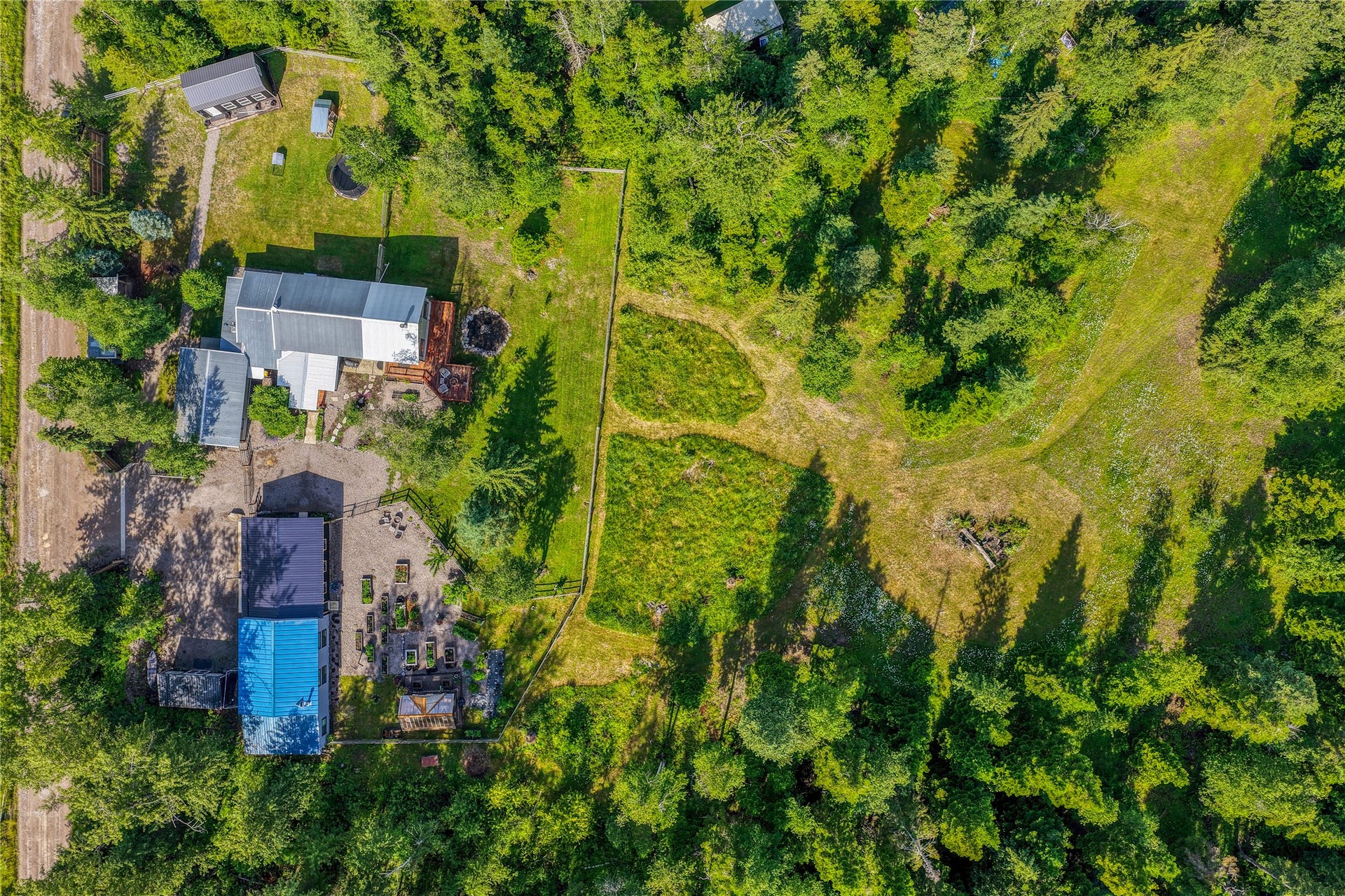 28012 Meadow Creek Road, Bigfork, MT 59911 Expansive property surrounded by dense evergreen foliage, featuring multiple structures including a main residence with a metal roof and an additional building with a blue metal roof