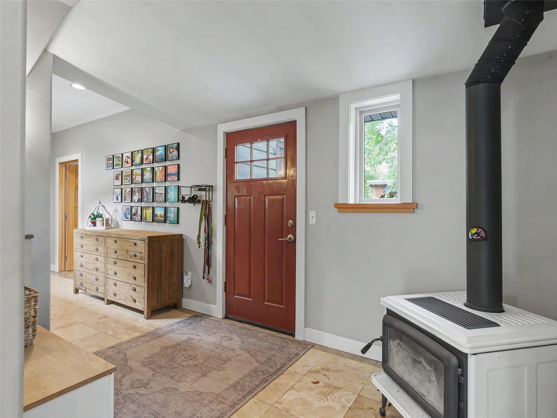 28012 Meadow Creek Road, Bigfork, MT 59911 Rear entry area featuring terra cotta tile flooring, a wood-burning stove with a black flue, and a red-paneled entry door with glass inserts
