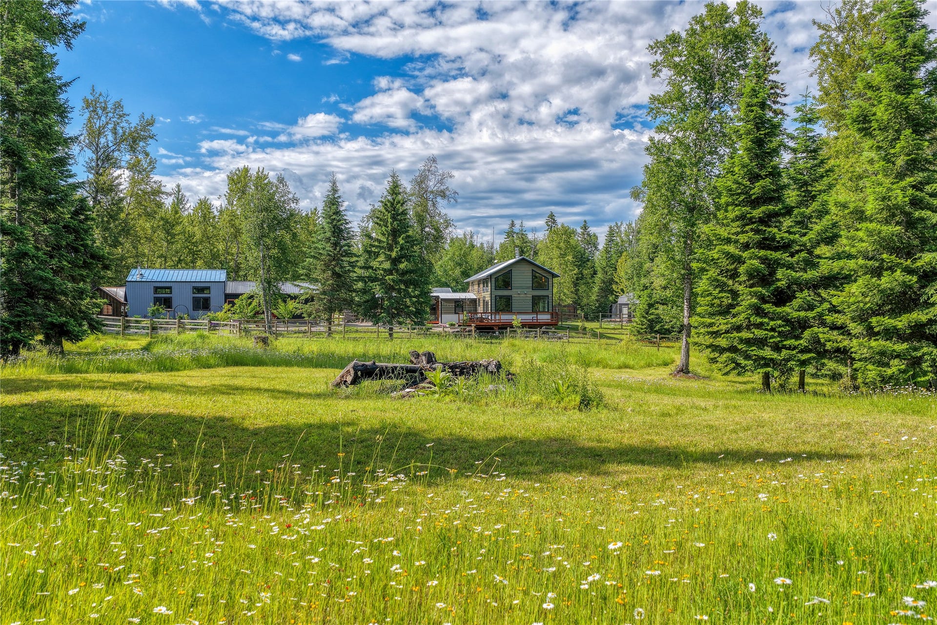 28012 Meadow Creek Road, Bigfork, MT 59911 Expansive green space featuring a natural grass field with wildflowers, mature evergreen trees, and a wooden fence