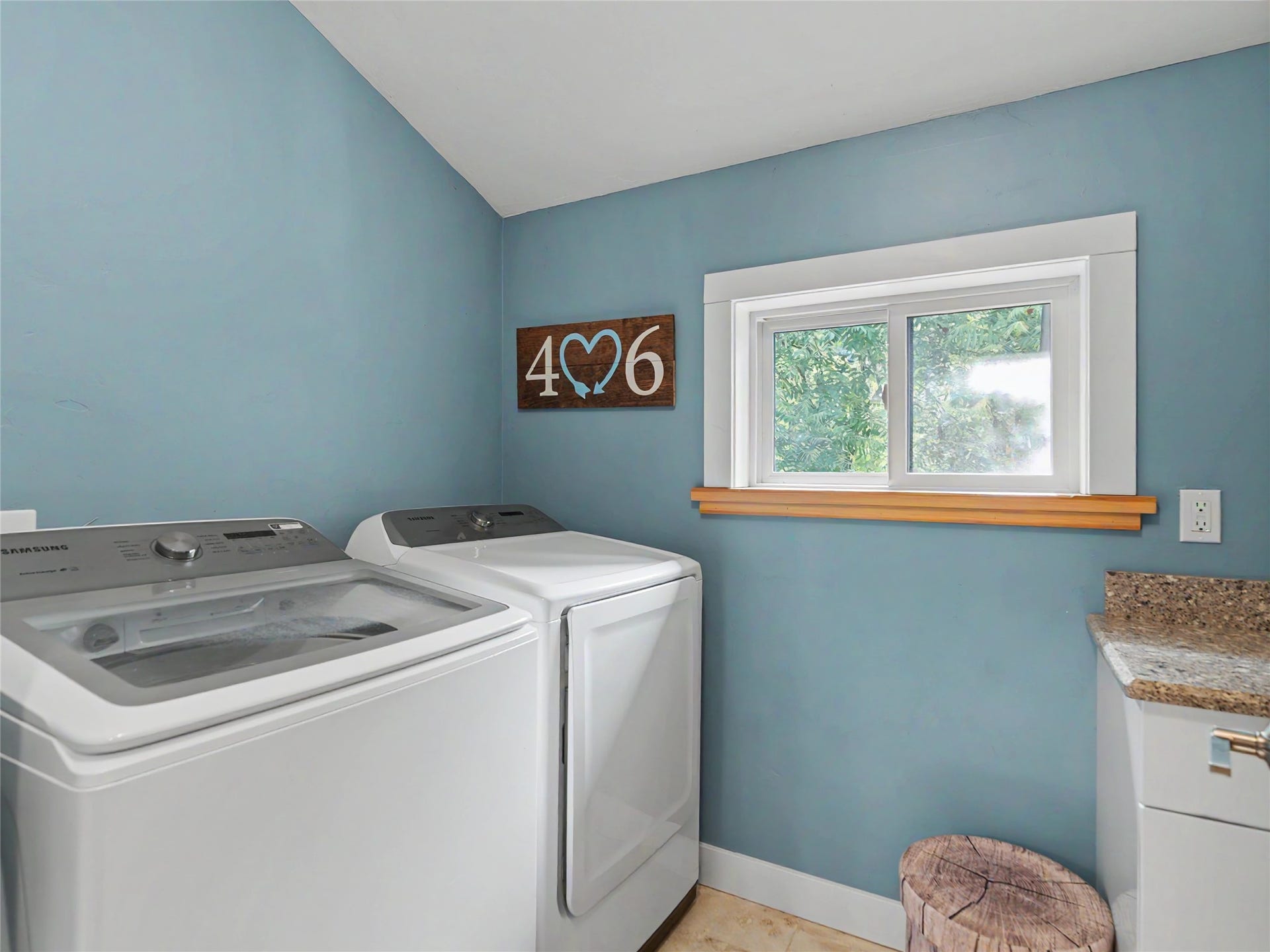 28012 Meadow Creek Road, Bigfork, MT 59911 Laundry area featuring a window with wood trim, blue painted walls, and a built-in cabinet with a speckled countertop