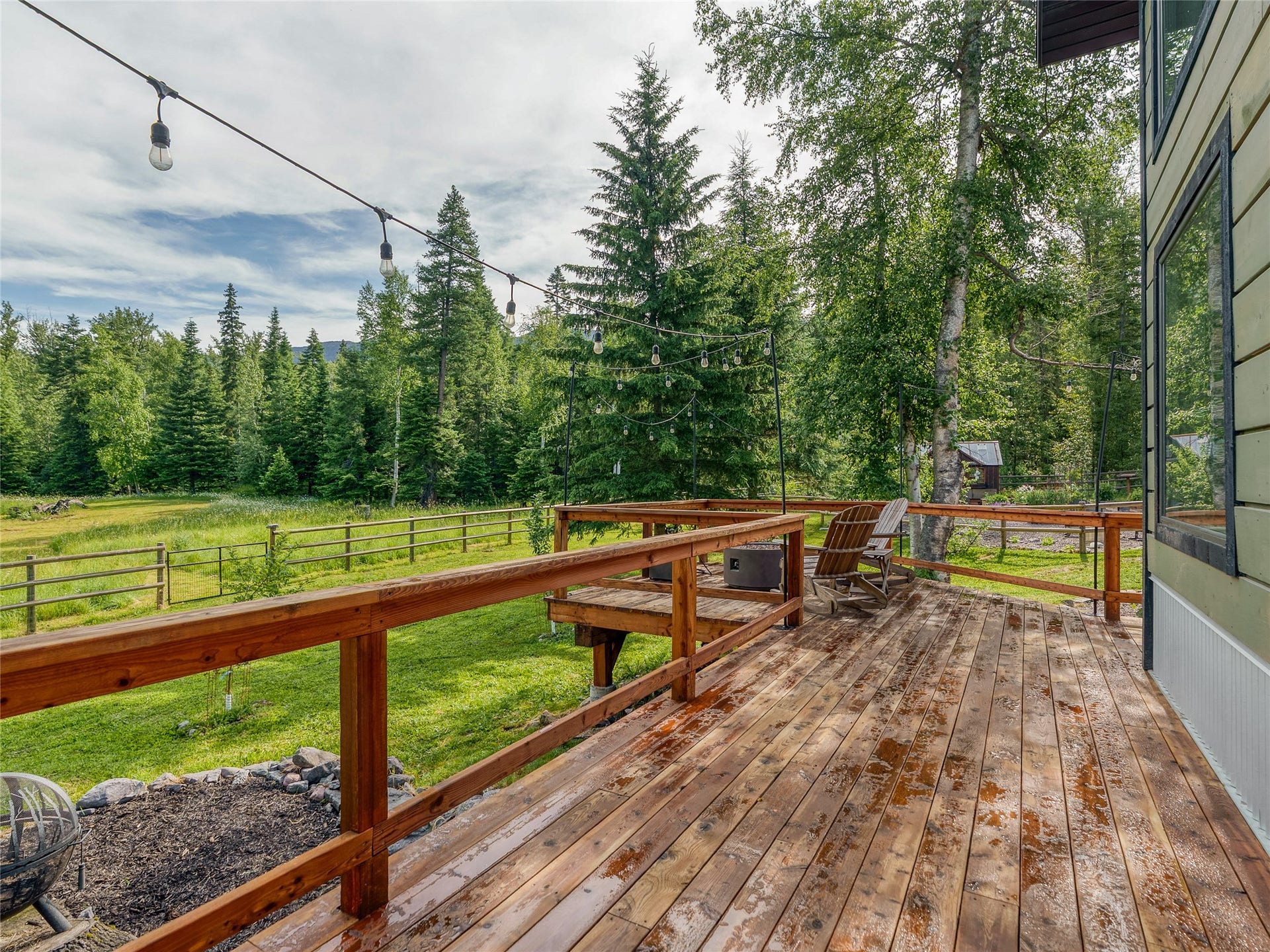 28012 Meadow Creek Road, Bigfork, MT 59911 Expansive wooden deck featuring string lighting, a wooden railing, and a fenced yard with mature trees