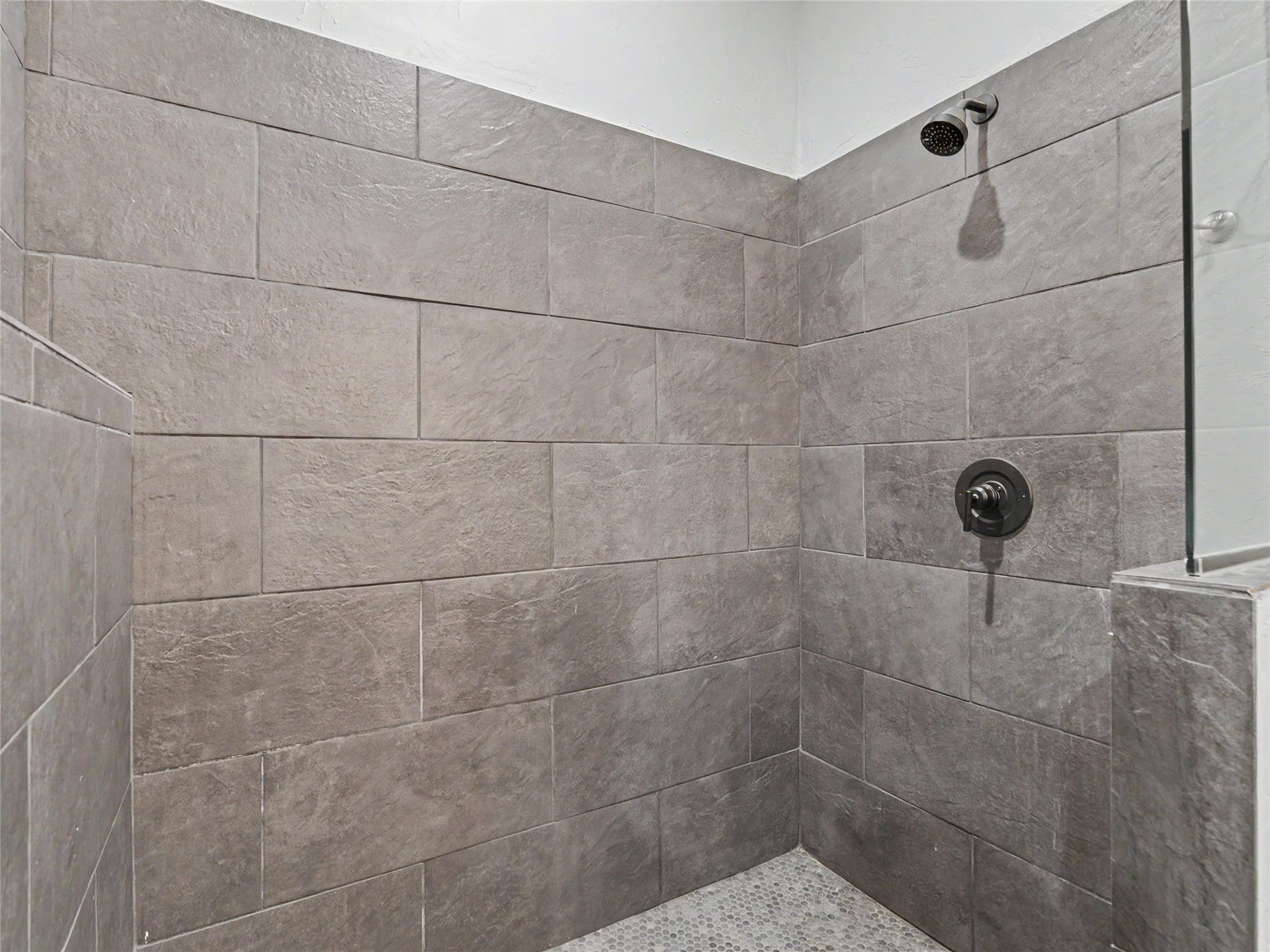 28012 Meadow Creek Road, Bigfork, MT 59911 Guest Quarters Shower enclosure featuring textured large format wall tiles, a mosaic tile floor, and matte black fixtures