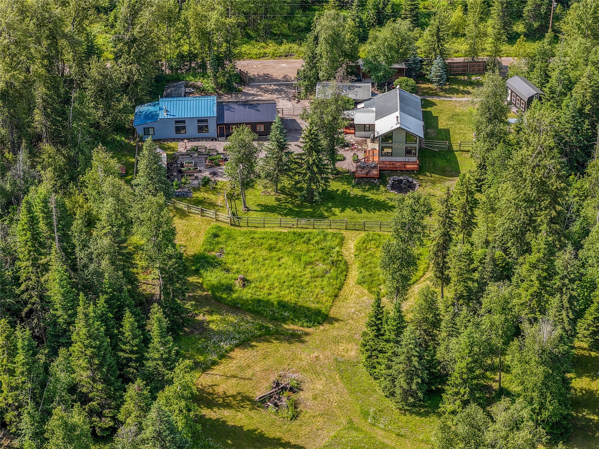 28012 Meadow Creek Road, Bigfork, MT 59911 Expansive forested property featuring multiple structures, including a primary residence with a large deck, a secondary dwelling with a blue metal roof, and a detached shed