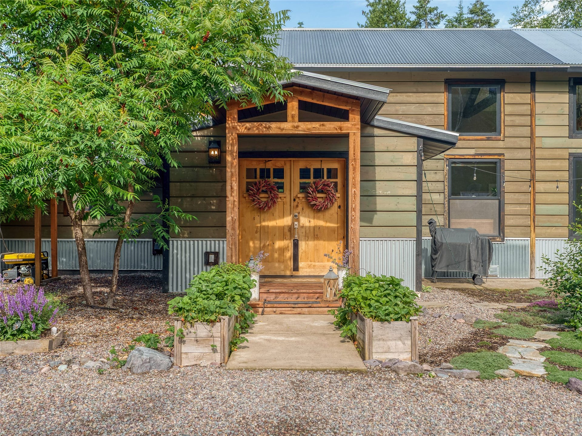 28012 Meadow Creek Road, Bigfork, MT 59911 Rustic modern facade featuring a wood-clad entry, double wooden doors, corrugated metal skirting, horizontal siding, and a metal roof