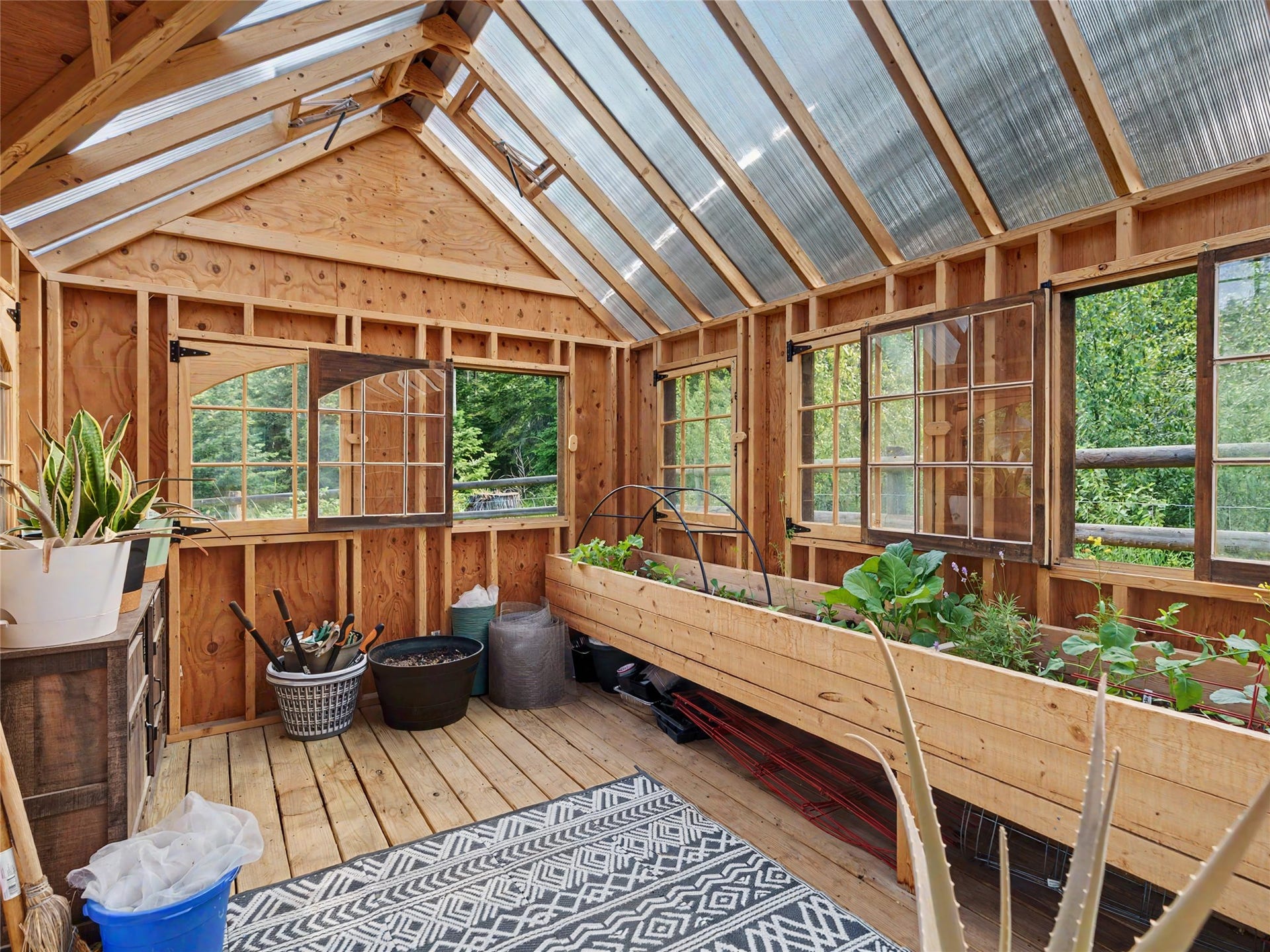 28012 Meadow Creek Road, Bigfork, MT 59911 Wood-framed greenhouse featuring a translucent panel roof, multiple operable windows, a built-in planter box, and wood-finish flooring