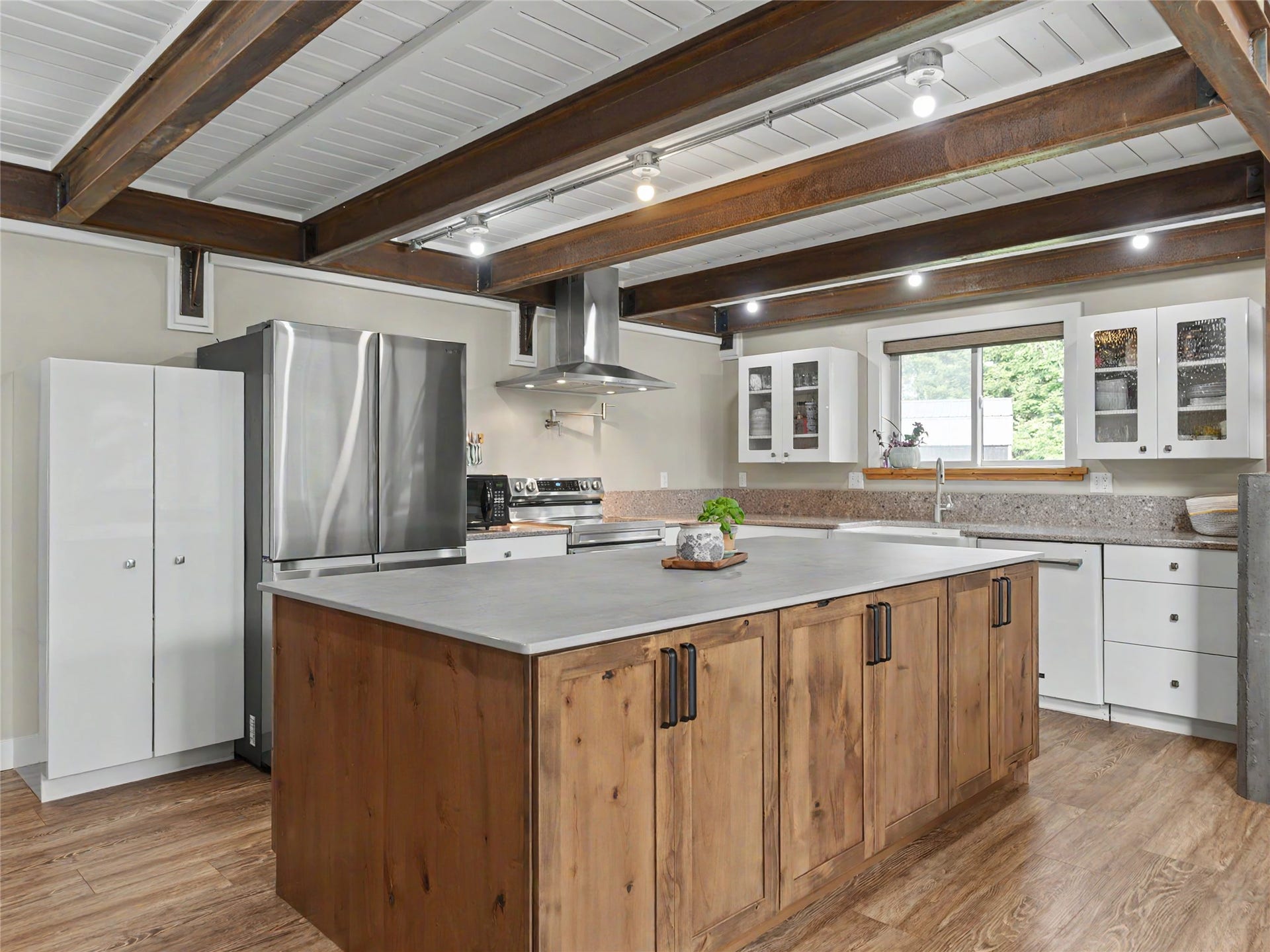 28012 Meadow Creek Road, Bigfork, MT 59911 Kitchen featuring a large central island with wood cabinetry, stainless steel appliances, white upper and lower cabinetry, and exposed ceiling beams