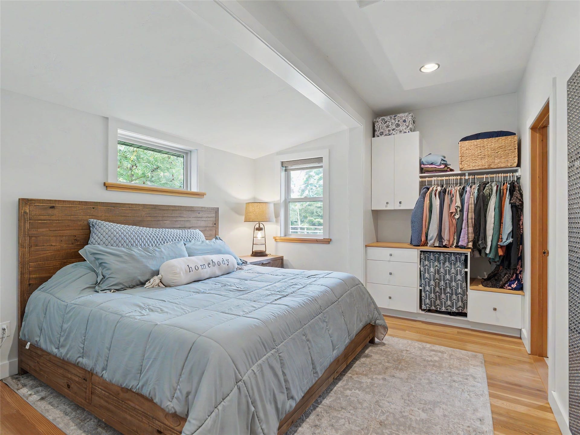 28012 Meadow Creek Road, Bigfork, MT 59911 Bright primary bedroom features a wood-frame bed, soft blue bedding, and hardwood flooring throughout