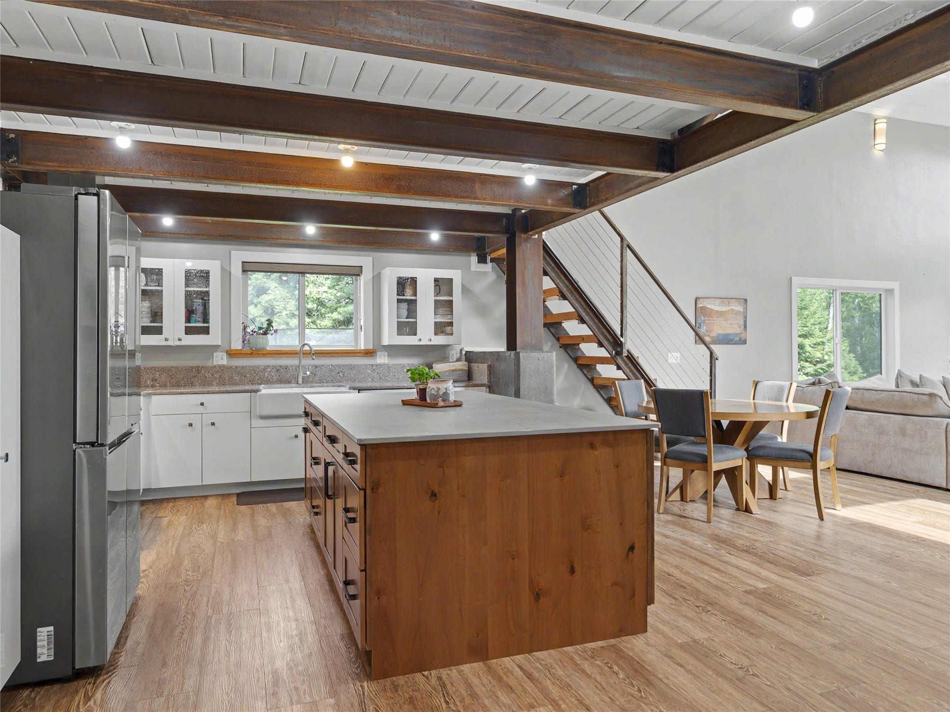 28012 Meadow Creek Road, Bigfork, MT 59911 Open-concept kitchen featuring a large wood-finish island, stainless steel refrigerator, white cabinetry with glass inserts, a farmhouse sink, and wood-finish flooring