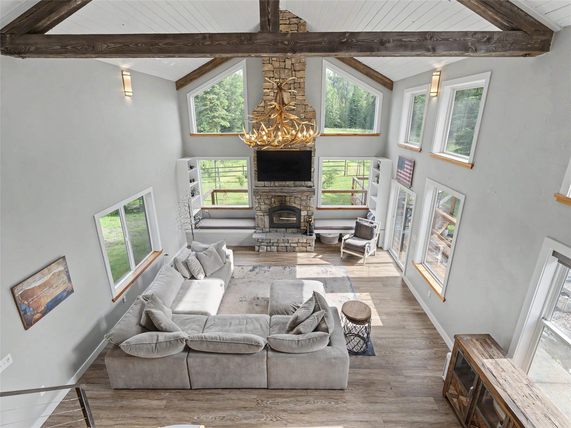 28012 Meadow Creek Road, Bigfork, MT 59911 Vaulted ceiling living space featuring exposed wood beams, a stone fireplace, wood-finish flooring, and multiple large windows with natural wood sills