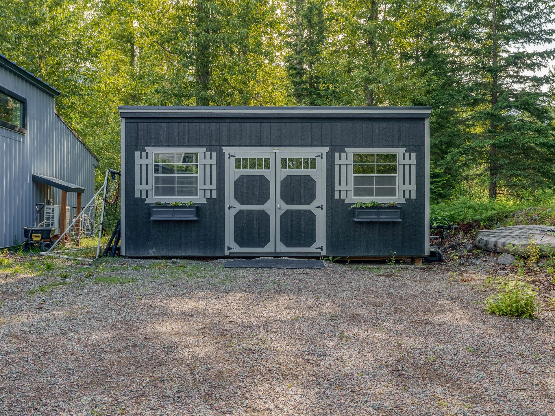 28012 Meadow Creek Road, Bigfork, MT 59911 Dark gray utility shed featuring white double doors, two white-framed windows with decorative shutters, and attached window boxes