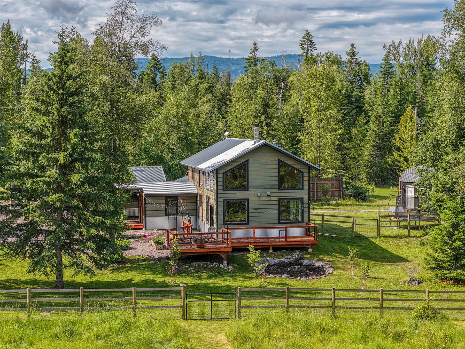 28012 Meadow Creek Road, Bigfork, MT 59911 Contemporary home with a dark green exterior siding, expansive window placements, and a natural wood-finish deck