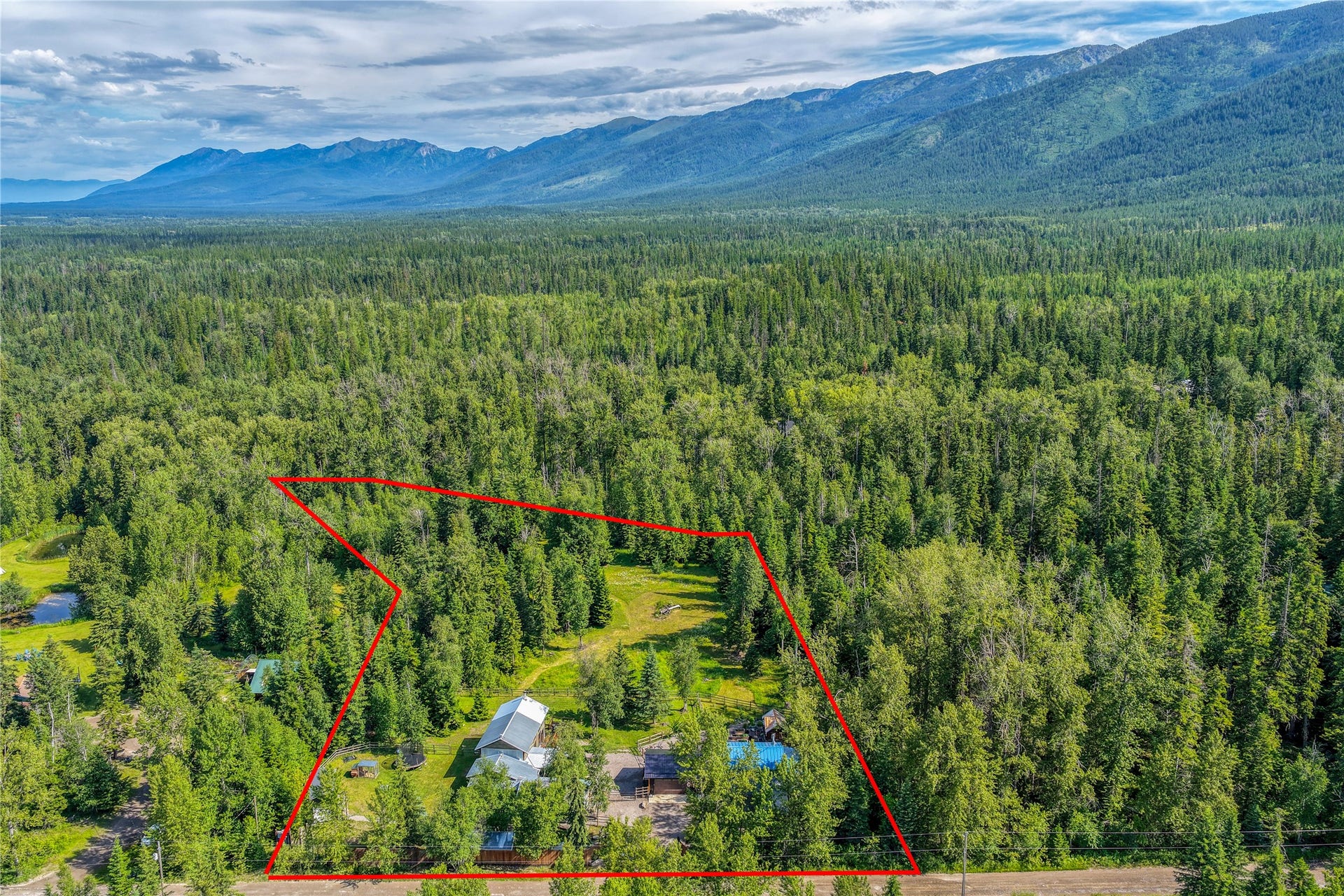 28012 Meadow Creek Road, Bigfork, MT 59911 Extensive treed acreage featuring a primary dwelling with a metal roof, a secondary structure, and a visible body of water