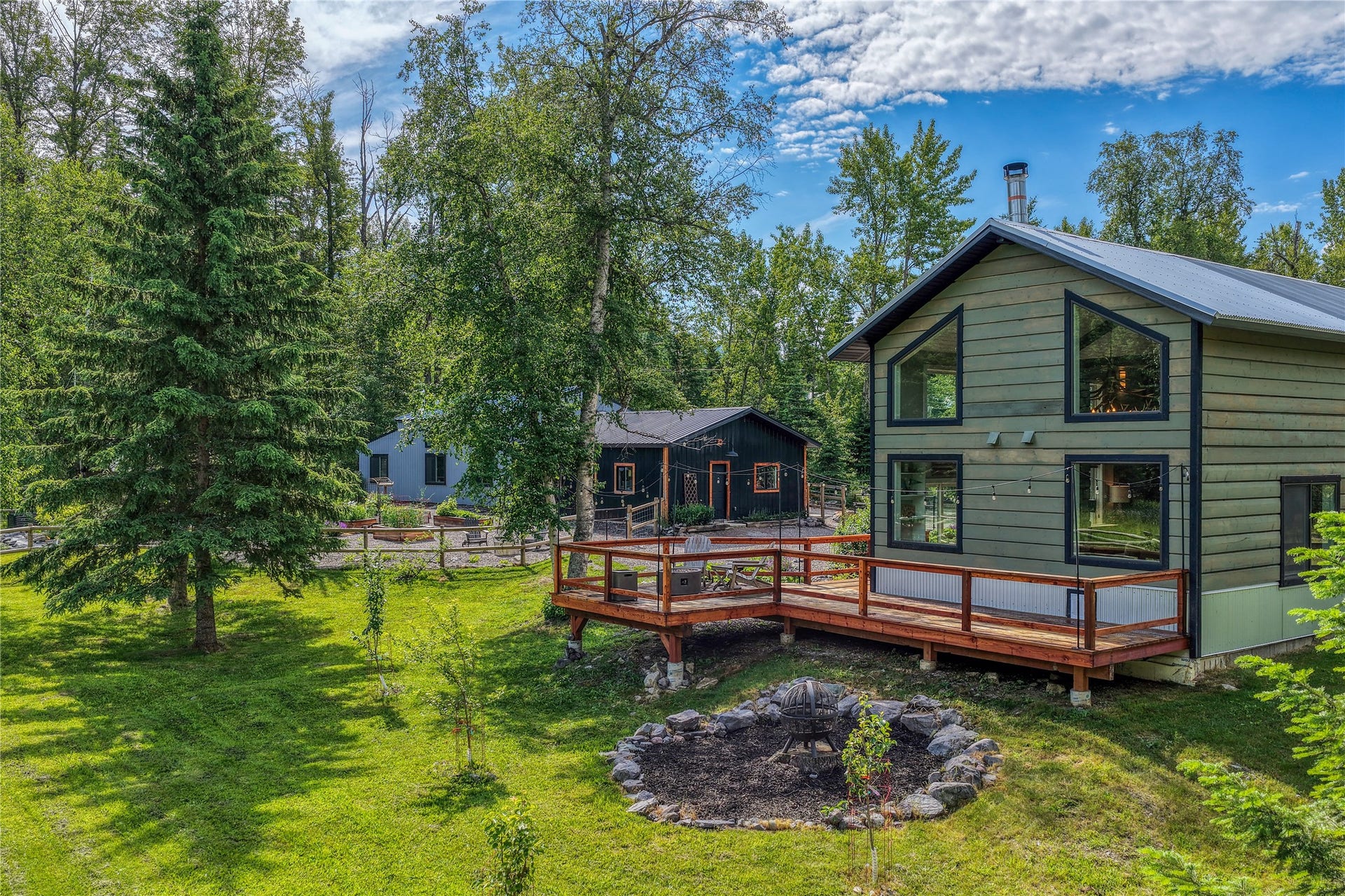 28012 Meadow Creek Road, Bigfork, MT 59911 Contemporary green exterior with large windows, a metal roof, and an expansive wood deck overlooking the back meadow toward the creek