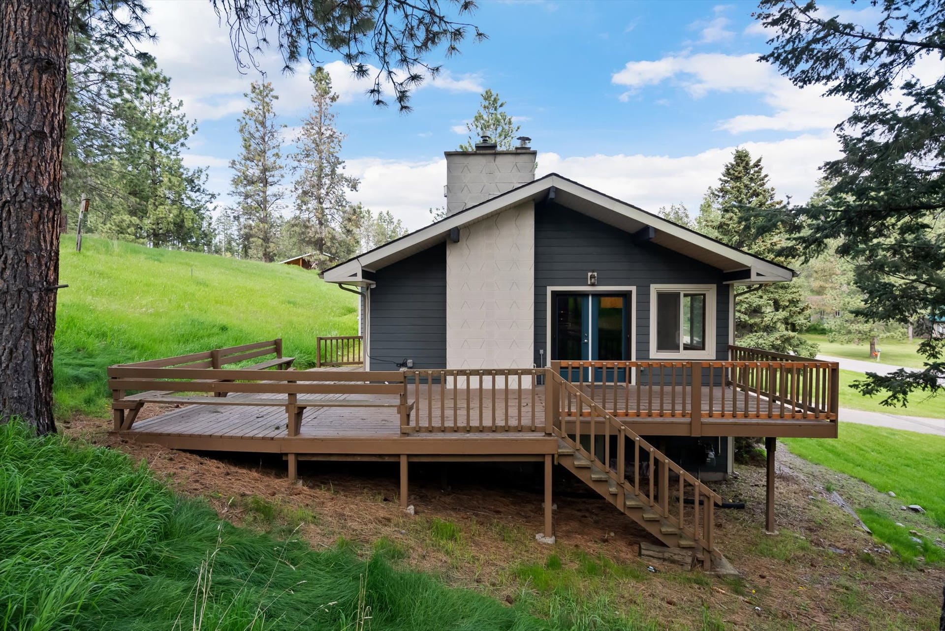 300 Peaceful Drive, Bigfork, MT 59911 Contemporary exterior featuring dark siding, a light-colored chimney, and a multi-level wood deck with railings