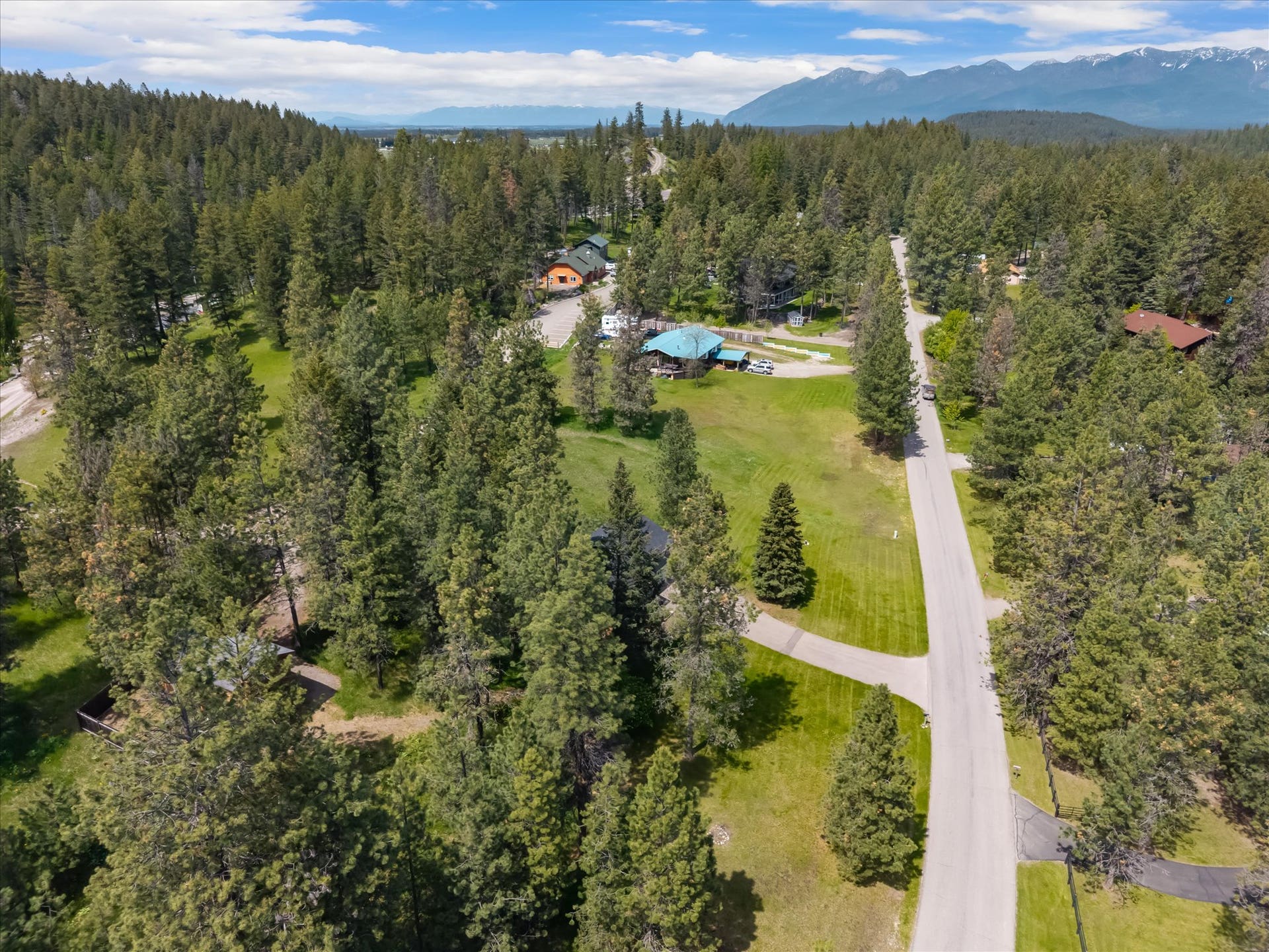 300 Peaceful Drive, Bigfork, MT 59911 Expansive treed parcel with a paved road, mountain backdrop, and multiple structures
