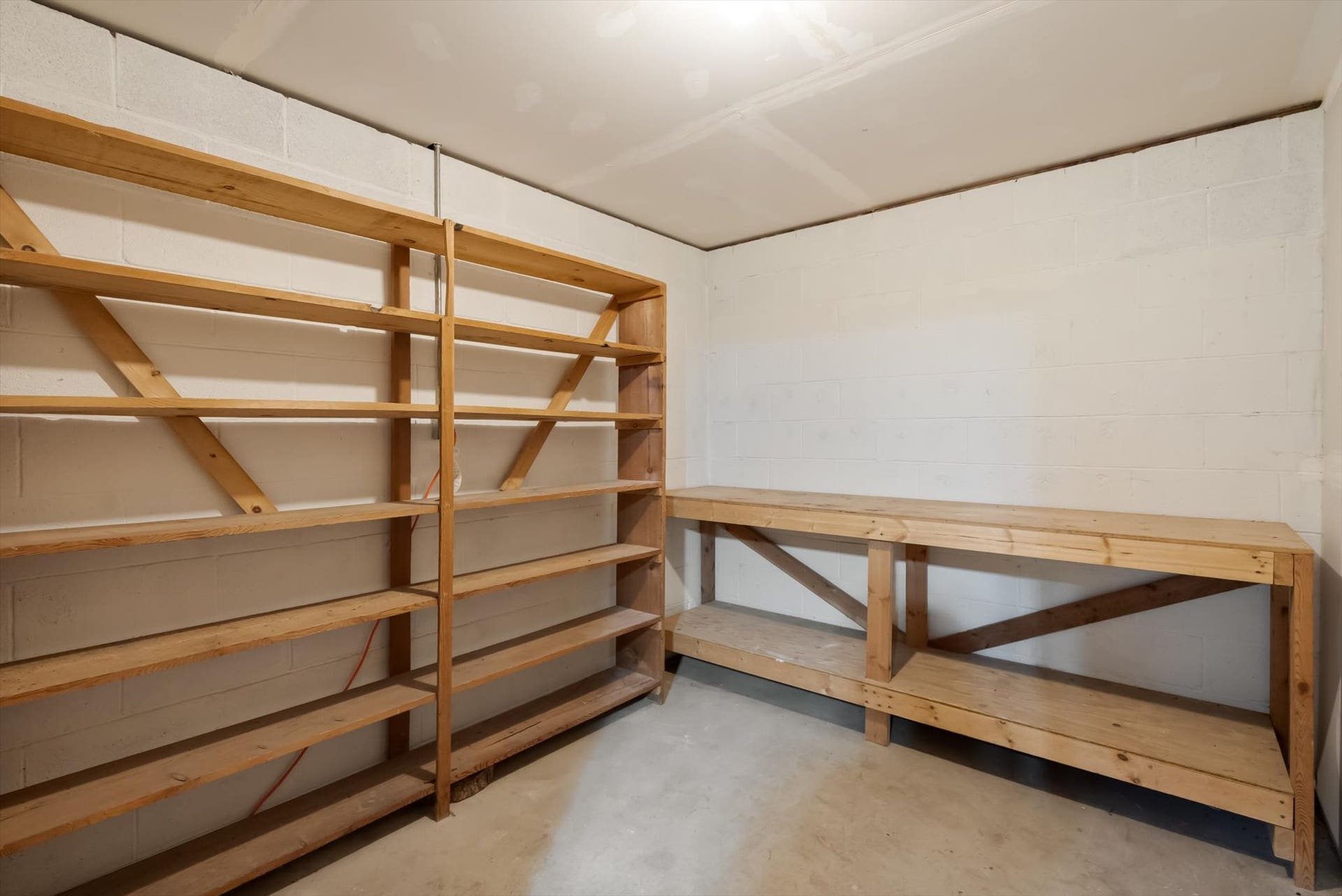 300 Peaceful Drive, Bigfork, MT 59911 Spacious utility room featuring extensive built-in wooden shelving, a long wooden workbench, white block wall construction, and a concrete floor