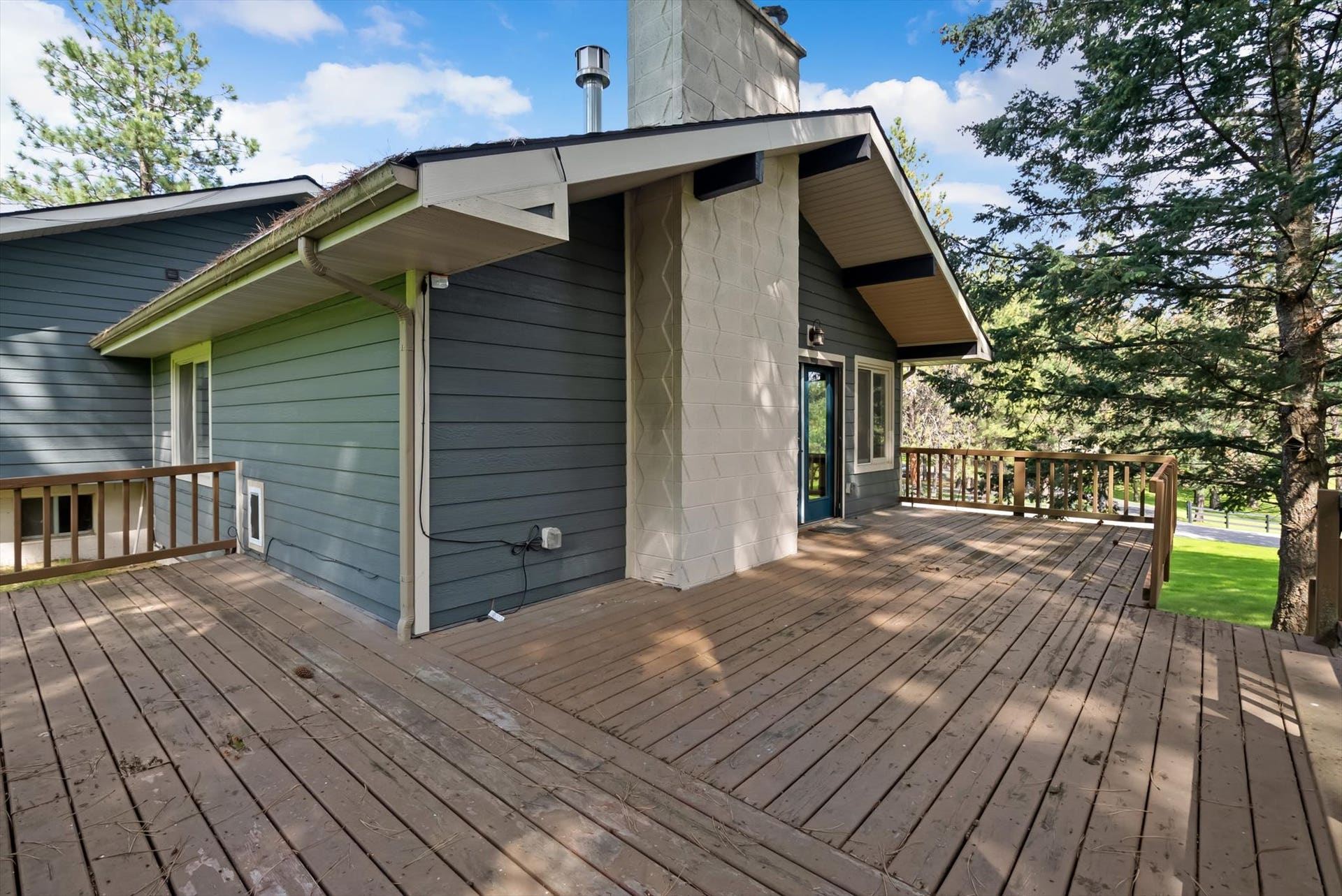 300 Peaceful Drive, Bigfork, MT 59911 Expansive wood deck with wood railings, framed by mature trees, complementing the property's siding and stone-finish chimney