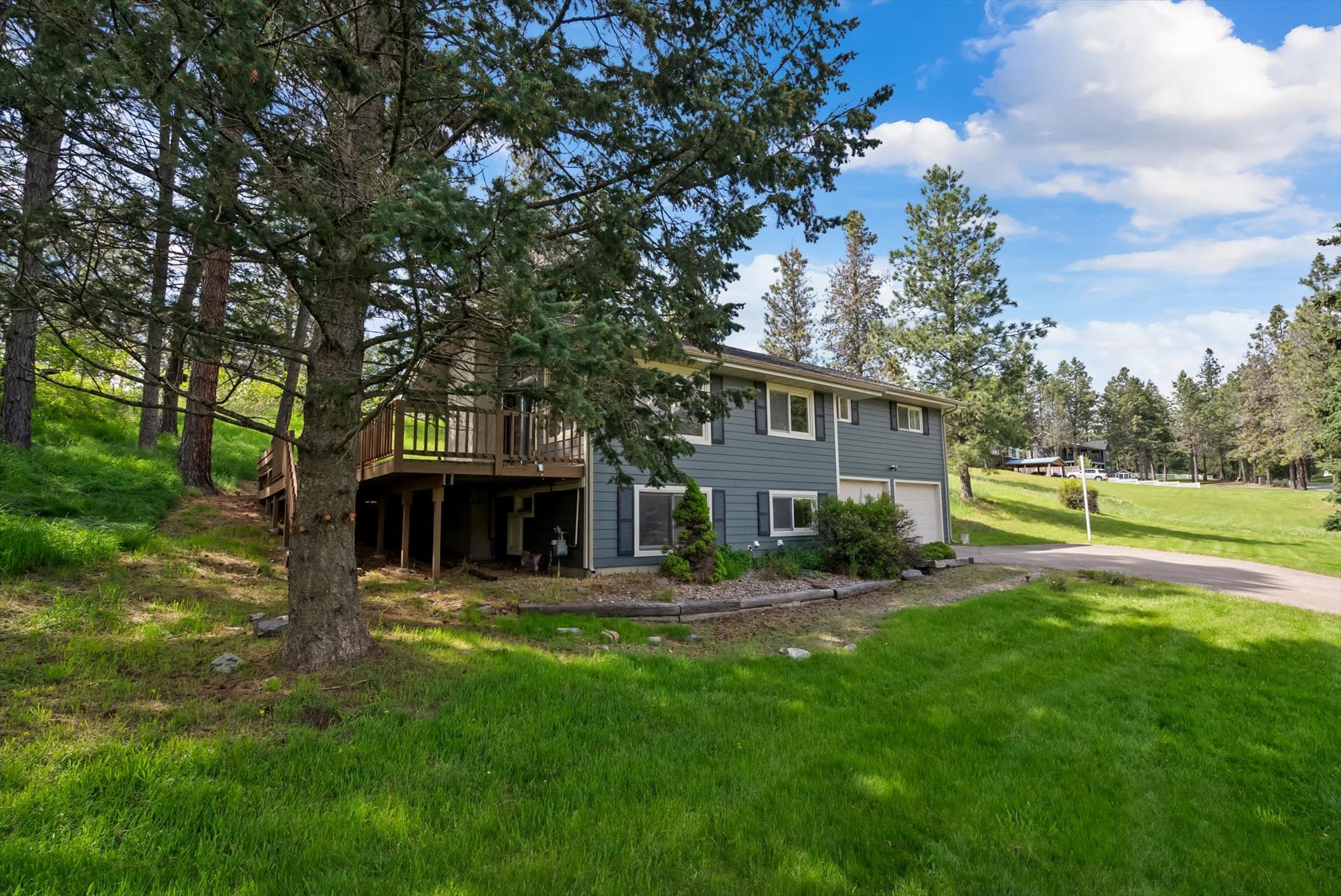 300 Peaceful Drive, Bigfork, MT 59911 Exterior featuring blue siding, multiple windows, an attached deck, and an integrated garage