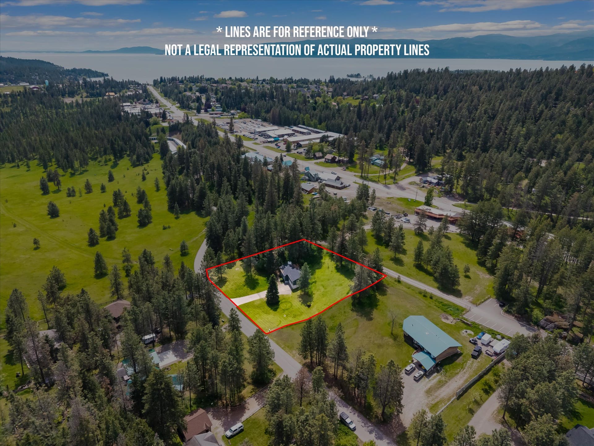 300 Peaceful Drive, Bigfork, MT 59911 Aerial perspective showcasing a property surrounded by mature trees, with a distant body of water and mountains