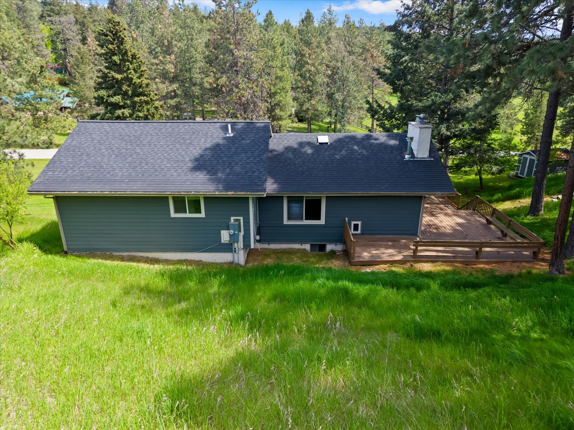 300 Peaceful Drive, Bigfork, MT 59911 Rear exterior featuring a spacious wooden deck with railings, a dark shingle roof, and a white-painted chimney
