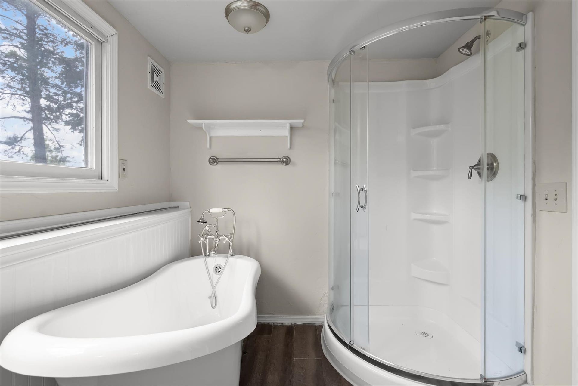 300 Peaceful Drive, Bigfork, MT 59911 Bathroom featuring a freestanding bathtub with classic faucet, a curved glass shower enclosure, wood-finish flooring, and a window providing natural illumination