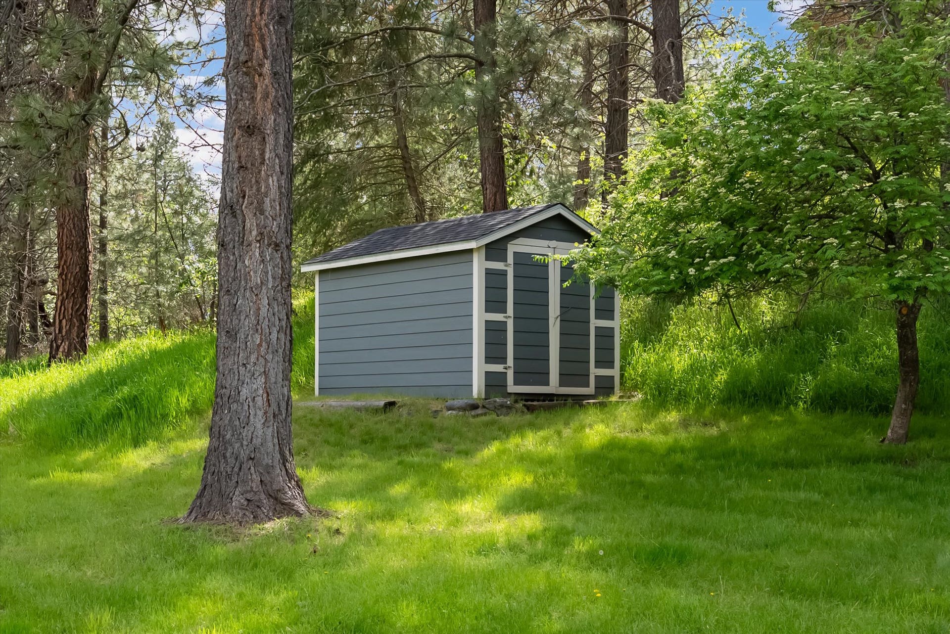 300 Peaceful Drive, Bigfork, MT 59911 Freestanding storage shed with horizontal siding, double doors, and a dark shingle roof, positioned on a grassy expanse among mature trees
