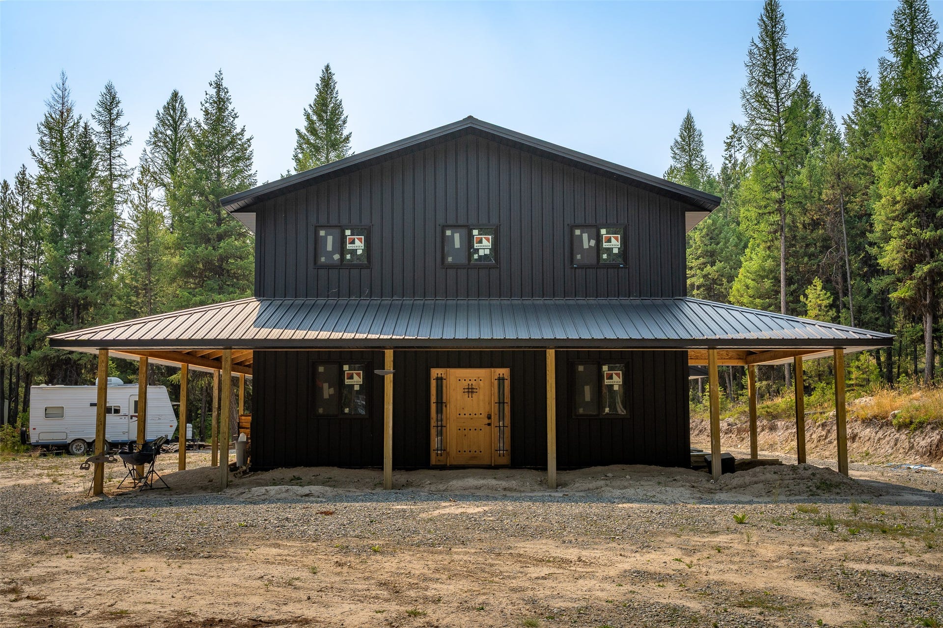 9653 Us Highway 2 W, Marion, MT 59925 Black corrugated metal siding with a metal roof, covered porch with natural wood posts, and a gravel perimeter