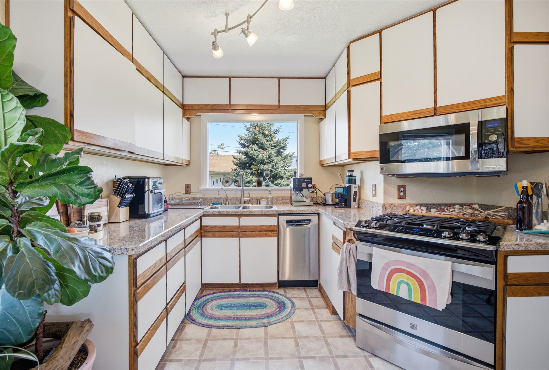 U-shaped kitchen with white cabinetry, wood-finish accents, granite-style countertops, stainless steel appliances, and a window above the sink