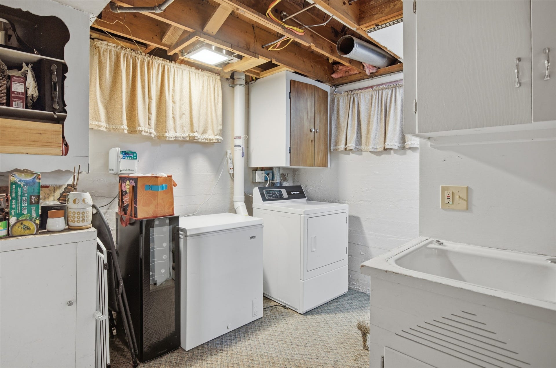 Basement utility area featuring a laundry sink, white cabinetry, and overhead exposed wood beams